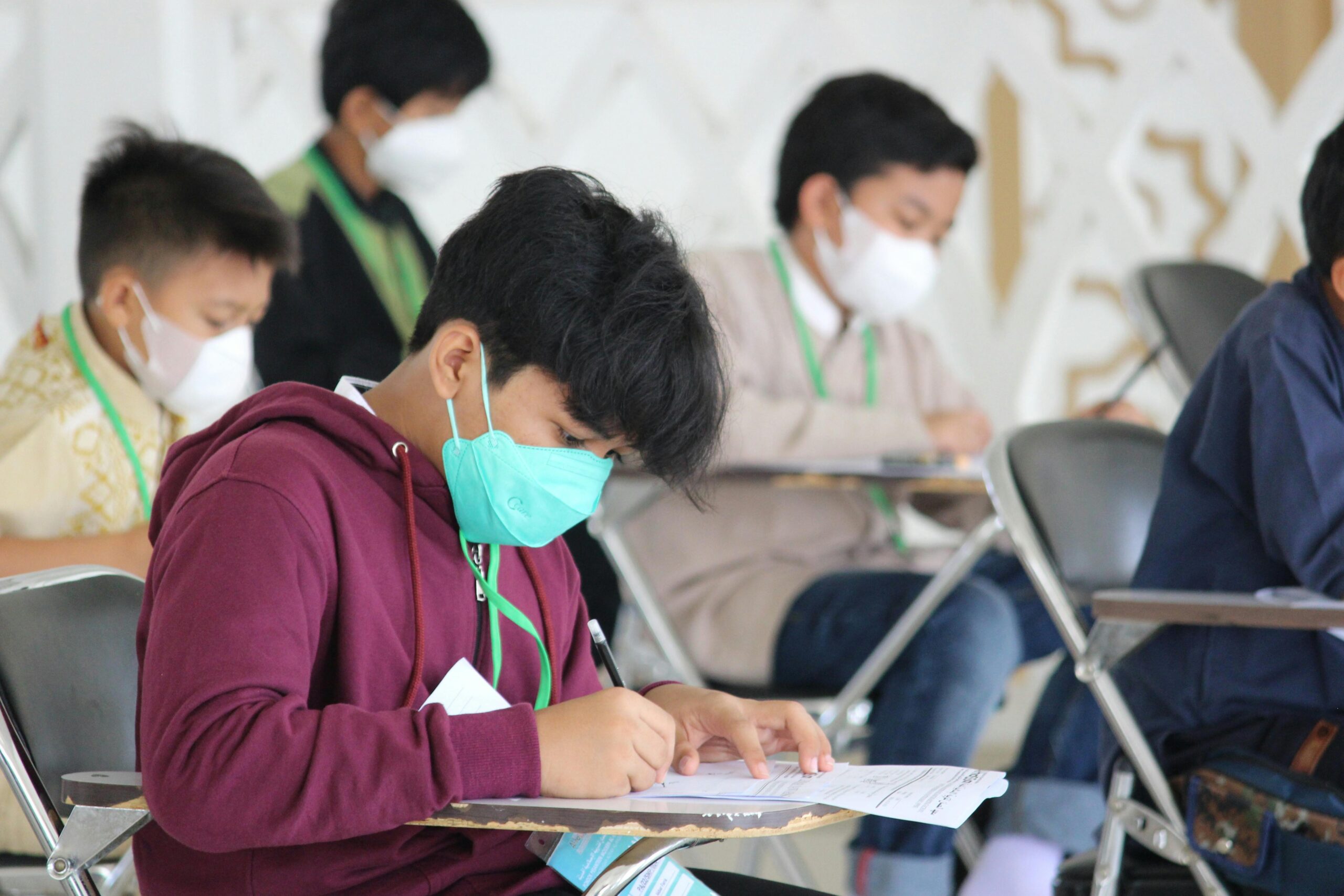 Teenagers wearing masks sit for an exam in an indoor setting, highlighting safety protocols.