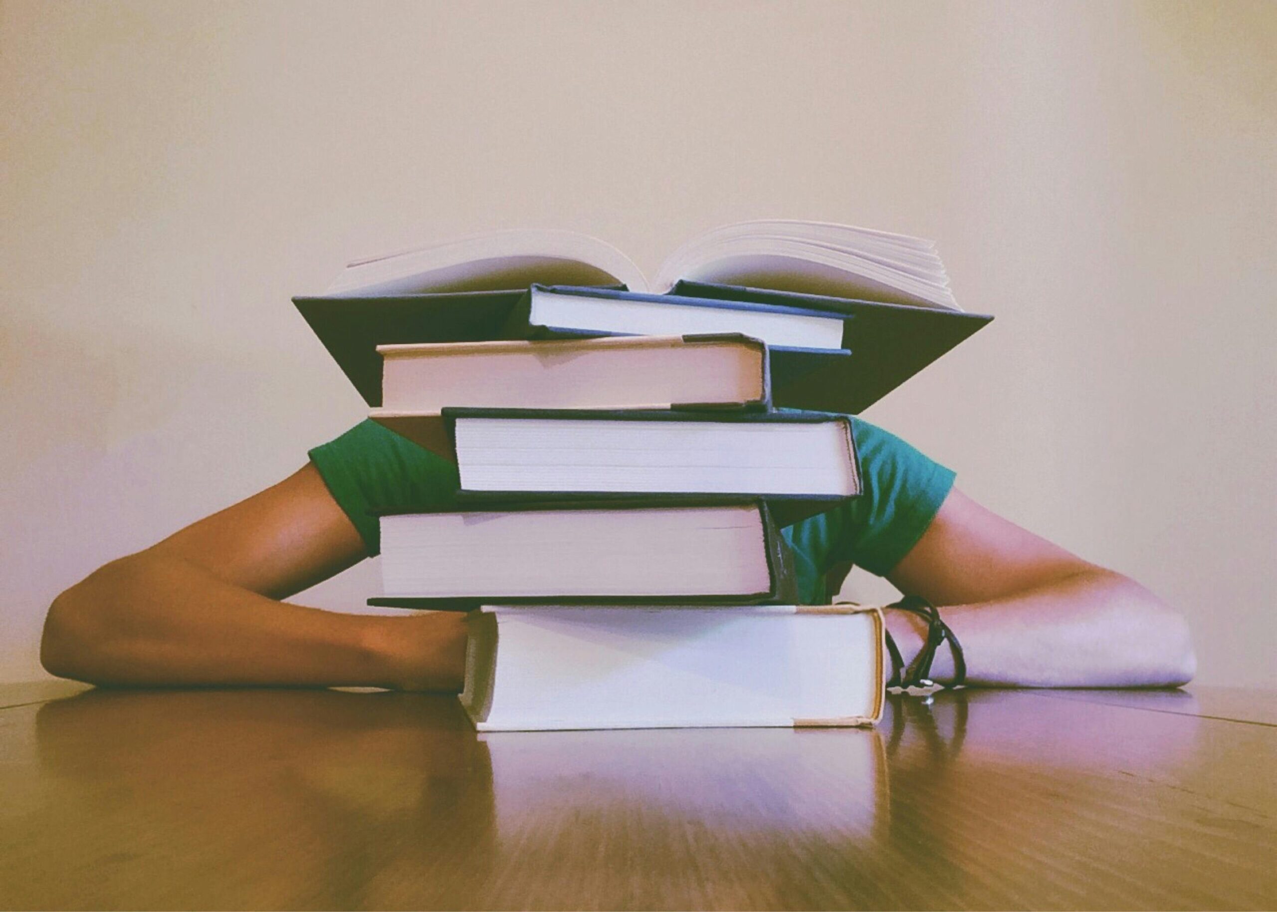 A student hidden behind a stack of books, symbolizing academic stress and study challenges.